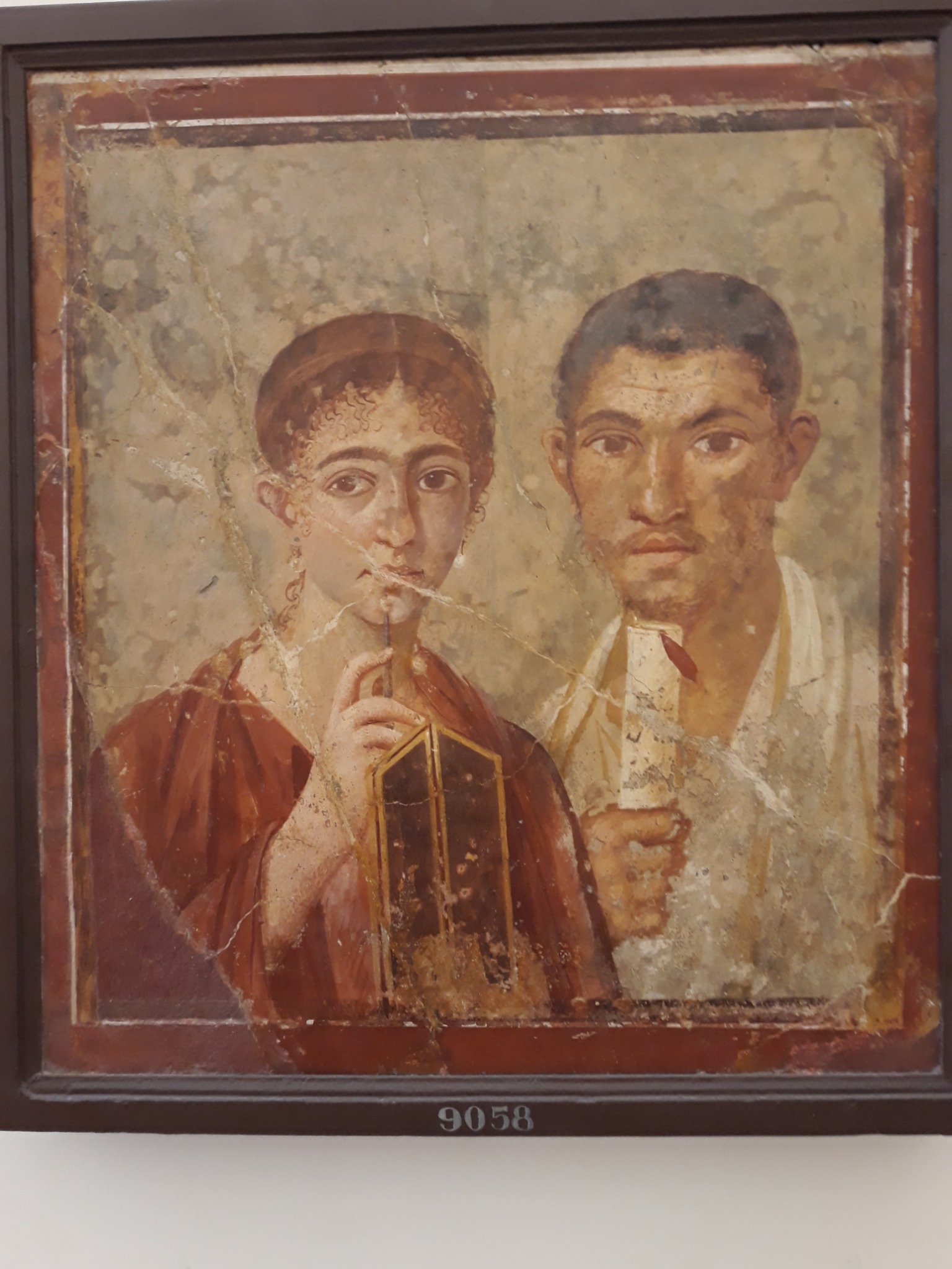 Pompeian woman holding wax tablets and a stylus beside a man holding a scroll.